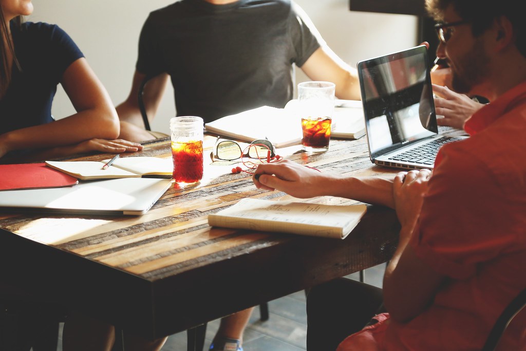 Vier Personen arbeiten gemeinsam an einem Holztisch mit Laptops und Notizbüchern.